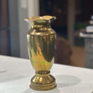 Puede incluir: Un jarrón de latón dorado con un borde acanalado y una base acampanada. El jarrón tiene un acabado liso y pulido.