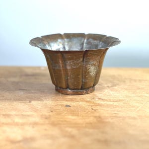 May include: A small, copper-colored metal planter with a fluted design. The planter has a slightly worn, aged look.