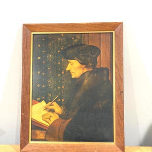 May include: A framed portrait of a man writing, with a dark hat and coat. The painting has a warm color palette, with a wooden frame. The background features a patterned wallpaper.