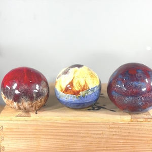 May include: Three spherical ceramic paperweights with glossy, multi-colored glazes. The left sphere features deep red and brown tones, the center sphere displays yellow, brown, and blue, and the right sphere shows a blend of red, blue, and purple.