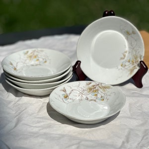 May include: Set of six white ceramic bowls with a floral design. The bowls have a delicate floral pattern in shades of brown and blue.
