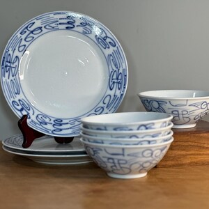May include: A set of blue and white ceramic bowls and plates with a decorative pattern. The bowls are stacked on top of each other and the plates are stacked on a wooden stand.