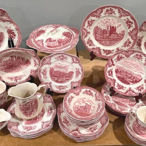 Puede incluir: Una colección de porcelana antigua roja y blanca con ilustraciones de castillos. El juego incluye platos, tazas, platillos, fuentes y una fuente cubierta. Los platos tienen bordes festoneados y un diseño detallado.
