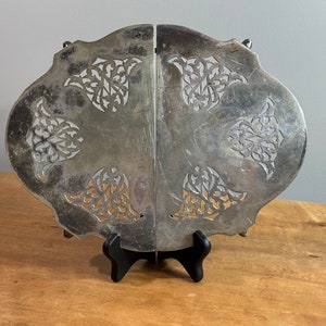 May include: A silver-plated, decorative, openwork serving tray with a scalloped edge and intricate floral designs. The tray is displayed on a black stand.