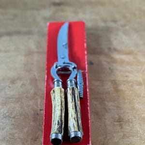 May include: A vintage nutcracker with a red box. The nutcracker has a silver blade and two antler-like handles.