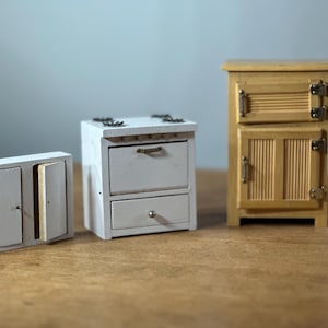 以下が含まれることがあります： 白と自然な木の色合いのミニチュア木製キャビネット3つ。左側のキャビネットは2つのドア、中央のキャビネットは2つの引き出し、右側のキャビネットは2つのドアです。