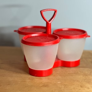 May include: Red plastic condiment holder with three clear containers and a handle. The containers have red lids.