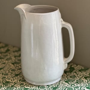 May include: A white ceramic pitcher with a wide mouth and a handle. The pitcher has a smooth, glossy finish.