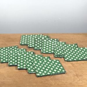 Könnte beinhalten: Eine Sammlung von quadratischen Untersetzern mit grünem und weißem Muster. Die Untersetzer sind auf einer Holzoberfläche angeordnet. Das Muster ist ein sich wiederholendes Rautenmuster. Die Untersetzer sind ein dekorativer Artikel für das Zuhause.