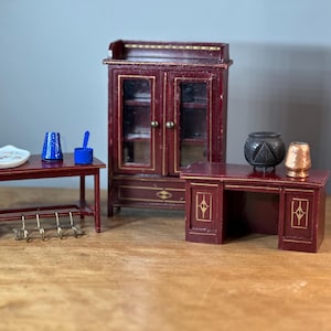 Pode incluir: Um conjunto de móveis em miniatura em um acabamento de madeira vermelho escuro. O conjunto inclui um armário com portas de vidro, uma escrivaninha com gavetas e uma mesa pequena com ganchos. Os móveis são decorados com detalhes dourados.