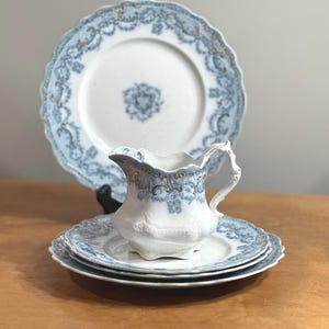 Może przedstawiać: Zestaw vintage porcelanowych talerzy w kolorze niebieskim i białym z delikatnym wzorem kwiatowym. Zestaw zawiera duży talerz, mniejszy talerz i dzbanek do śmietanki.
