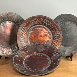 May include: Four antique copper plates with intricate designs. The plates are arranged in a semi-circle on a wooden surface.