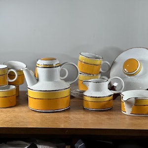 May include: A vintage tea set with a white base and yellow and brown stripes. The set includes a teapot, creamer, sugar bowl, and six cups.