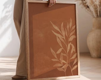 Pode incluir: Uma impressão de arte emoldurada com um design botânico. A obra de arte tem um fundo de terracota quente com um padrão de folhas bege claro. A moldura é feita de madeira de cor clara, adicionando um toque natural à peça.