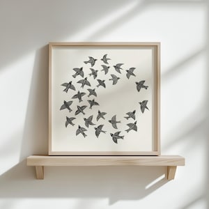 May include: A framed print showing a flock of black birds in a circular formation on a cream background. The artwork is displayed on a light wooden shelf, creating a minimalist aesthetic. The frame and shelf are made of light-colored wood.