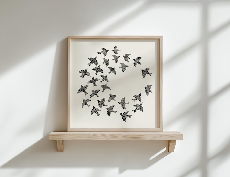 May include: A framed print showing a flock of black birds in a circular formation on a cream background. The artwork is displayed on a light wooden shelf, creating a minimalist aesthetic. The frame and shelf are made of light-colored wood.