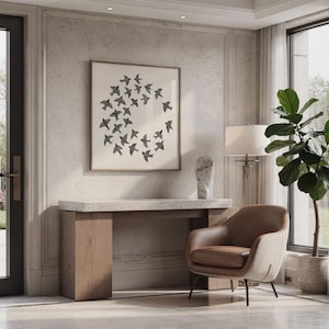 May include: A framed print showing a circular arrangement of black birds. The artwork is above a wooden console table with a marble top. A brown leather armchair and a potted plant are also in the room.