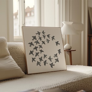 May include: A framed canvas print showing a circular arrangement of black bird silhouettes against a neutral background. The artwork is set within a wooden frame. The piece is displayed on a beige sofa.