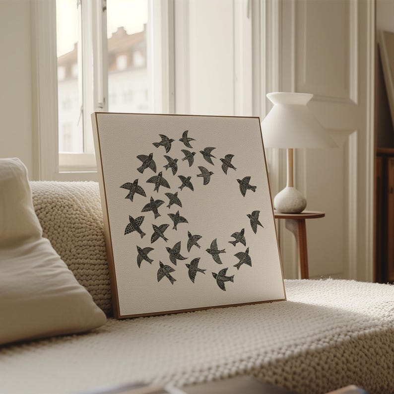 May include: A framed canvas print showing a circular arrangement of black bird silhouettes against a neutral background. The artwork is set within a wooden frame. The piece is displayed on a beige sofa.