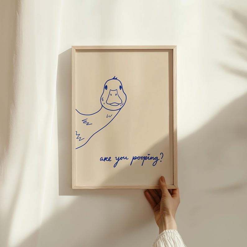 May include: A framed print featuring a whimsical blue line drawing of a duck. The duck is peeking from the side, with the text "are you pooping?" written below in a matching blue script. The frame is a light wood color.