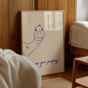 May include: A framed art print featuring a whimsical blue line drawing of a duck. The duck is drawn with a simple, cartoonish style. The text "are you pooping?" is written in blue script below the duck.
