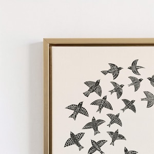 May include: A framed canvas print showing a flock of black birds flying on a cream background. The birds have detailed wing patterns. The frame is a warm gold colour, adding a touch of elegance to the artwork.
