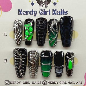 May include: A set of press-on nails with various designs, including silver swirls, green accents, and black and silver patterns. The nails are displayed on a white card with the text "Nerdy Girl Nails" and social media handles.