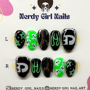 Puede incluir: Un juego de uñas postizas Nerdy Girl Nails. Las uñas presentan varios diseños, incluyendo llamas verdes, fantasmas blancos y un diseño en blanco y negro con las letras "BP". Las uñas son de forma ovalada y se muestran en una tarjeta blanca.
