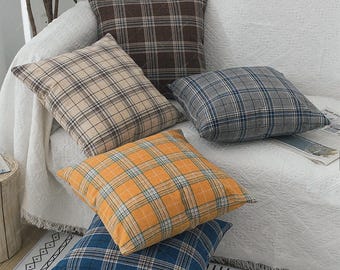 Op de afbeelding: Een verzameling van vijf vierkante sierkussens met diverse ruitpatronen in tinten donkerbruin, beige, grijs met blauwe accenten, mosterdgeel en diepblauw. Elk kussen heeft een zichtbaar gestikt ruitontwerp en een zachte textuur.
