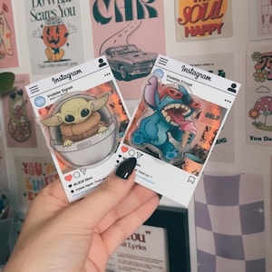 Puede incluir: Dos pegatinas con temática de Instagram se sostienen en una mano. Una presenta a Grogu de The Mandalorian, y la otra a Stitch de Lilo & Stitch. Las pegatinas tienen un fondo transparente y están rodeadas de otros carteles decorativos.