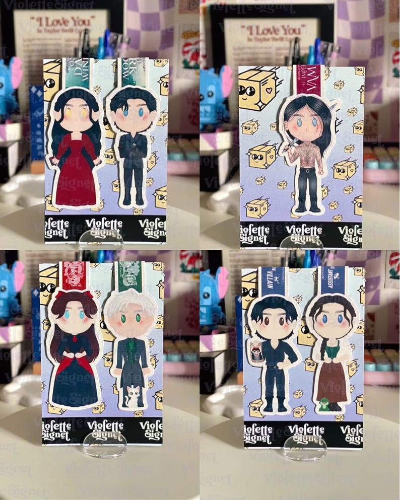 May include: Four character-themed bookmarks with cartoon illustrations. Each bookmark features a different pair of characters, with a purple background and the text "Violette Signet". The bookmarks are displayed on clear stands.