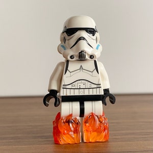 Puede incluir: Una minifigura Lego Star Wars Stormtrooper blanca con una visera negra y detalles azules en el casco. La minifigura está de pie sobre un par de llamas Lego naranjas.