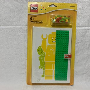 May include: A yellow LEGO minifigure with a green LEGO minifigure behind it. The minifigures are on a white background with a green LEGO brick pattern on the right side. The image is on a yellow and white LEGO notebook cover. The cover says "LEGO" and "Notebook".