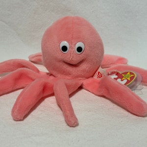 May include: Pink plush octopus with white eyes and a smiling mouth. The octopus has eight tentacles and is holding a red and yellow "Ty" tag with a star.