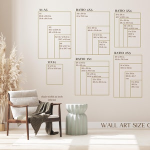 May include: A wall art size guide with different ratios and measurements in inches and centimetres. The guide shows the dimensions of various sizes of wall art, including 11x14, 4x5, 3x4, 2x3, and 1x1 ratios. The guide is displayed on a wall with a light beige colour. A chair with a light beige fabric and a light green stool are in the foreground.