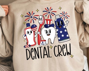May include: A beige sweatshirt with a graphic of a toothbrush, toothpaste, and a tooth wearing a red, white, and blue hat. The graphic is surrounded by fireworks and the text "Dental Crew".