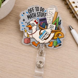 Peut inclure: Un porte-badge à paillettes représentant un canard de dessin animé portant des lunettes et tenant un crayon. Le texte indique OFF TO DO MATH STUFF et CUSTOM NAME. Le design inclut une calculatrice, un panier d'outils mathématiques et des formes.