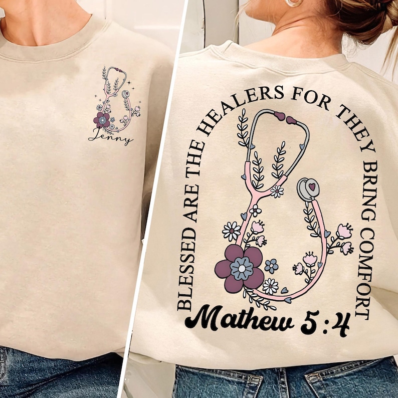 May include: Beige sweatshirt with a stethoscope and floral design. The front features a small stethoscope graphic with the name "Jenny". The back has a larger stethoscope design with the text "Blessed are the healers for they bring comfort" and "Mathew 5:4".