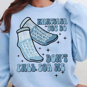 Puede incluir: Sudadera azul claro con un gráfico de dos calcetines azules y el texto "Whatever you do don't fall for me" en una fuente retro.