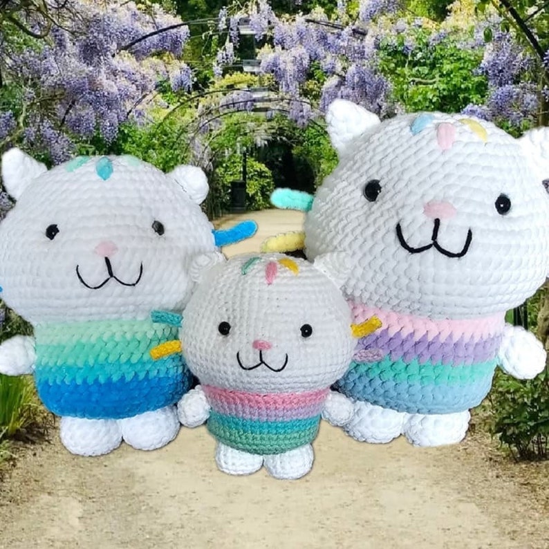 Peut inclure: Trois poup&eacute;es chats en crochet blanc avec des yeux noirs et des nez roses. Les poup&eacute;es ont une moiti&eacute; inf&eacute;rieure aux couleurs de l'arc-en-ciel et de petits accents color&eacute;s sur la t&ecirc;te. Les poup&eacute;es sont de tailles variables, la plus grande &eacute;tant &agrave; droite.