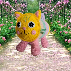 Peut inclure: Une poup&eacute;e chat au crochet faite &agrave; la main, avec une t&ecirc;te jaune, des joues roses et des yeux noirs. Le corps est ray&eacute; de couleurs pastel et les pattes sont roses. Le chat est sur un chemin avec des p&eacute;tales de fleurs roses.