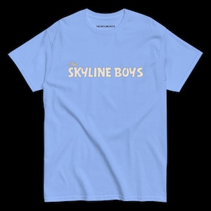 Puede incluir: Camiseta azul claro con el texto "The SKYLINE BOYS" en una fuente retro en el pecho. El texto "THE SKYLINE BOYS" también está impreso en la parte superior de la camiseta. La camiseta es de un material suave.