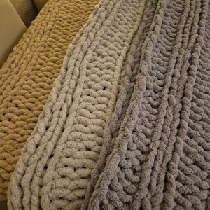 May include: Three chunky knit blankets in beige, light gray, and dark gray. The blankets are made with thick yarn and have a cable knit pattern.