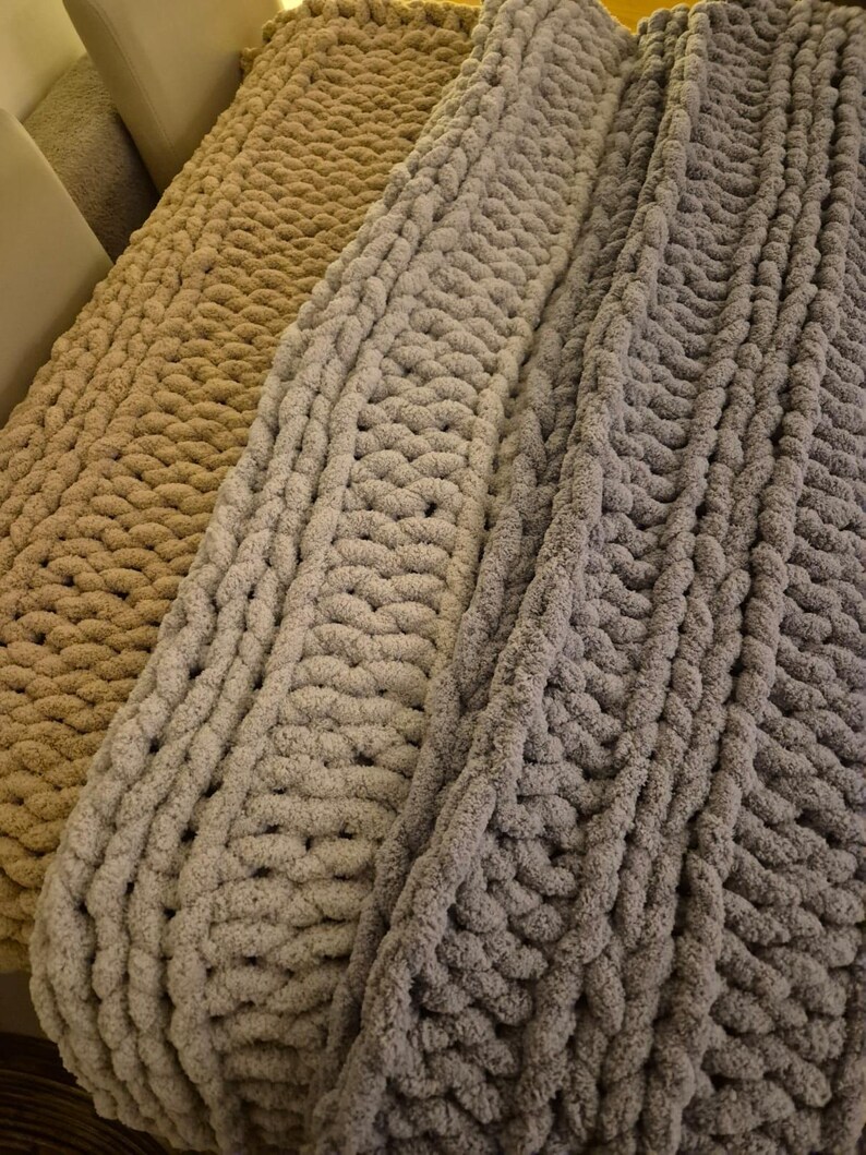 May include: Three chunky knit blankets in beige, light gray, and dark gray. The blankets are made with thick yarn and have a cable knit pattern.