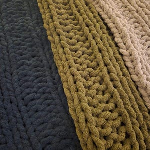 May include: Three chunky knit blankets in different shades of green. The blankets are made with thick yarn and have a textured, cable knit pattern.