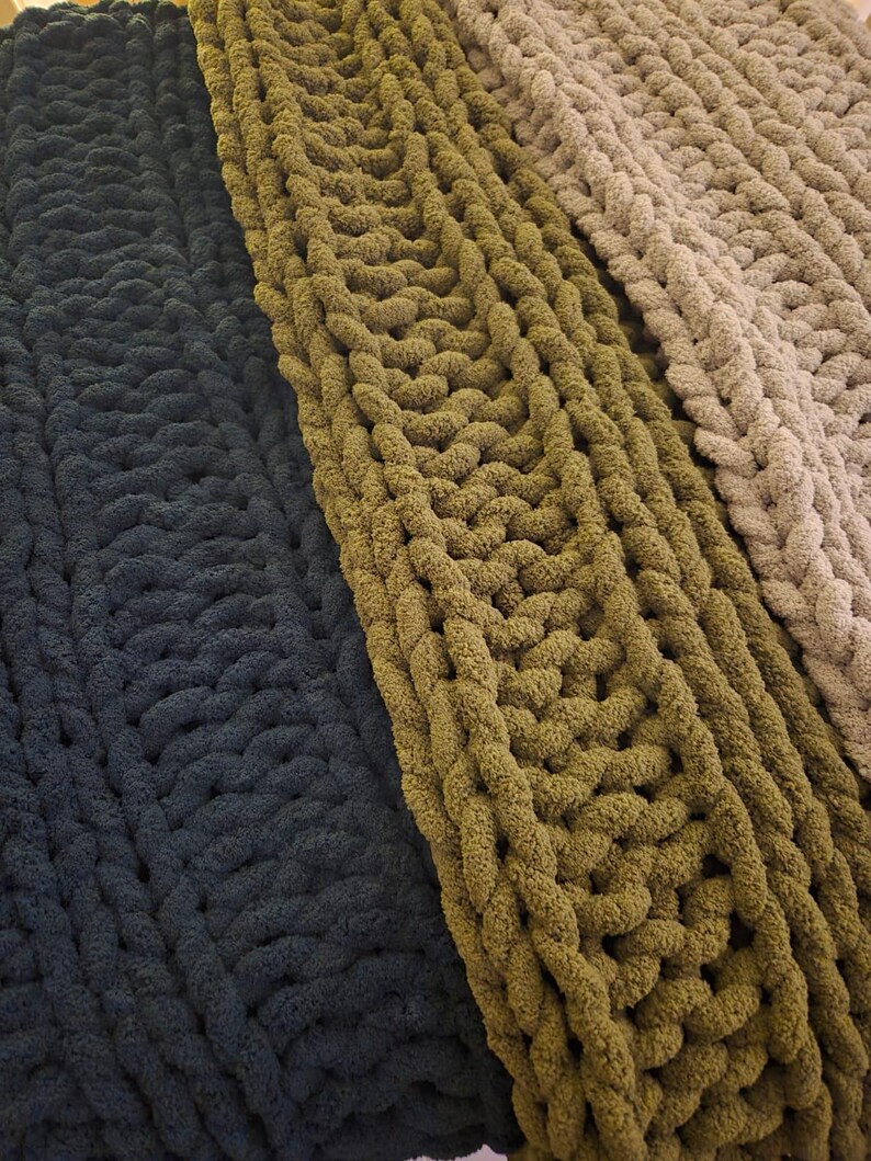 May include: Three chunky knit blankets in different shades of green. The blankets are made with thick yarn and have a textured, cable knit pattern.