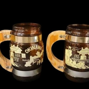 May include: Four brown glass mugs with wooden handles. Each mug has a silver band around the top and a gold design with the text "Okinawa" and "Naha" on the front.