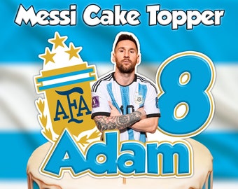May include: A blue and white cake topper featuring a soccer player, the number 8, and the name Adam. The soccer player is wearing a blue and white jersey with the Argentina national team logo. The cake topper also includes the Argentina Football Association logo.