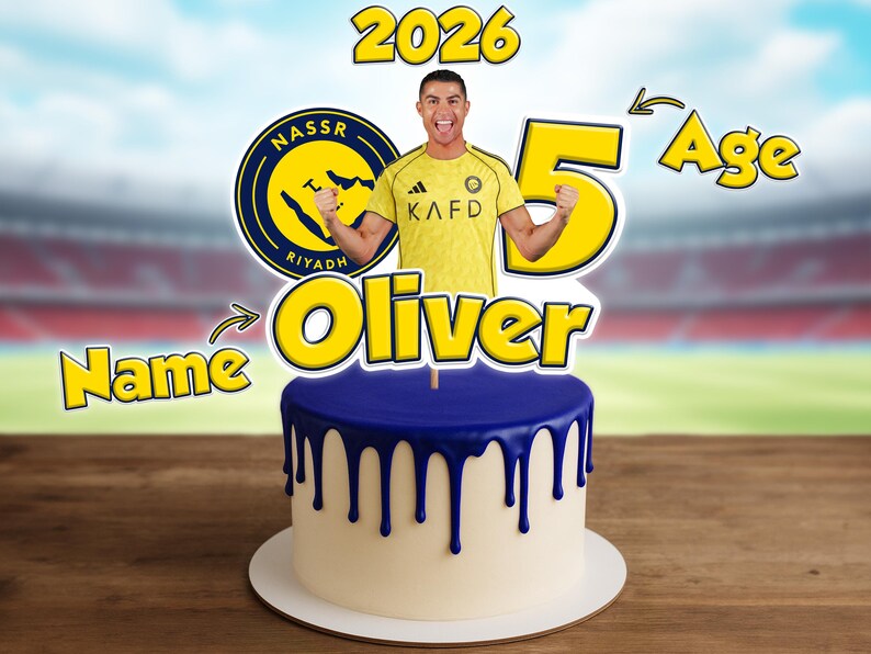 May include: A birthday cake with blue icing drips, featuring a cutout of a soccer player and the name "Oliver". The number "5" and the year "2026" are also displayed. The cake is on a wooden surface.