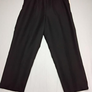 以下が含まれることがあります： 黒色のワイドレッグパンツ、ウエストはゴム入り、ハンガーに吊るされています。パンツは無地の濃い色の生地で作られています。脚はストレートで、床まで届きます。